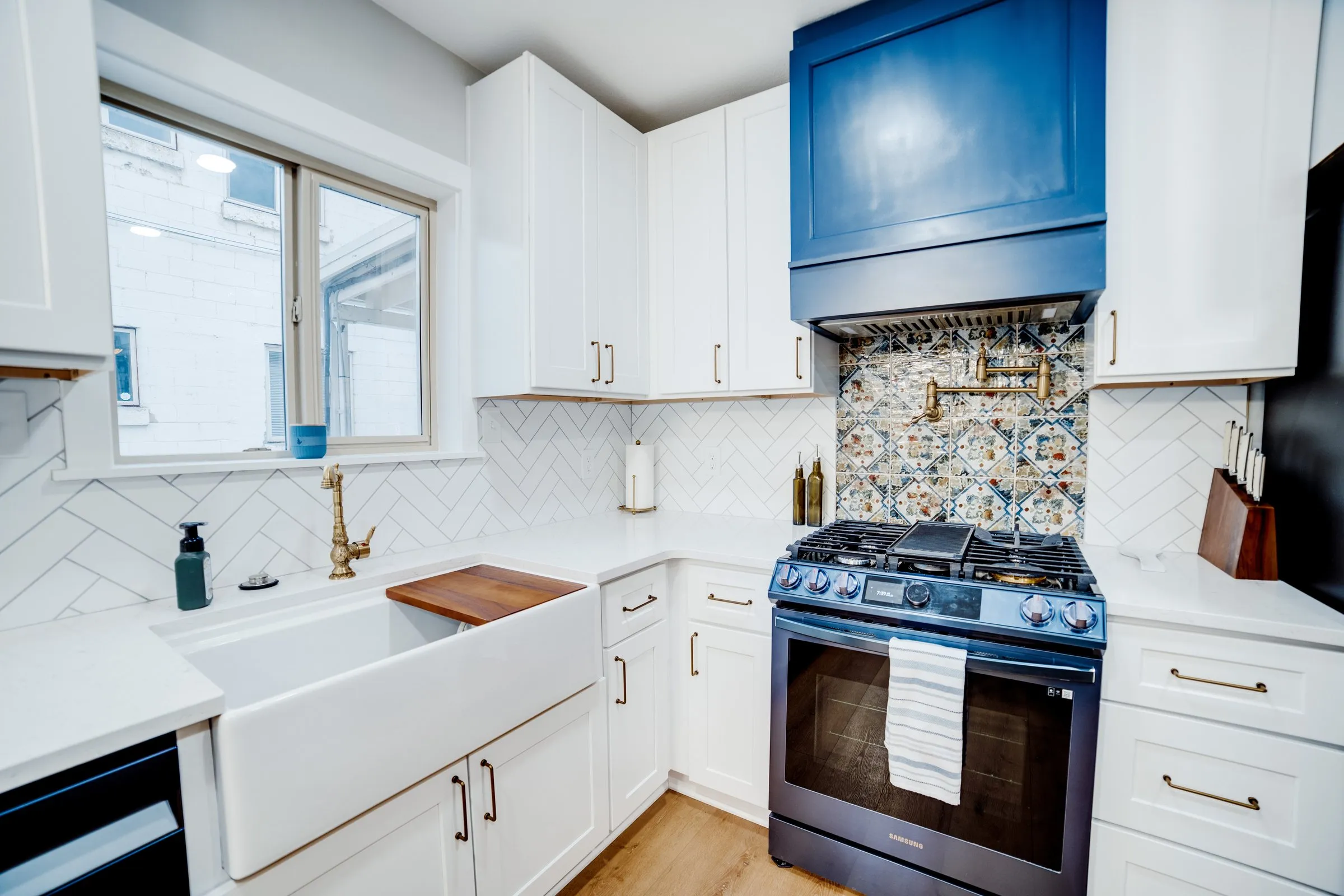 Chef’s kitchen with gas range, navy range hood, patterned tile backsplash and farmhouse sink with brass faucet