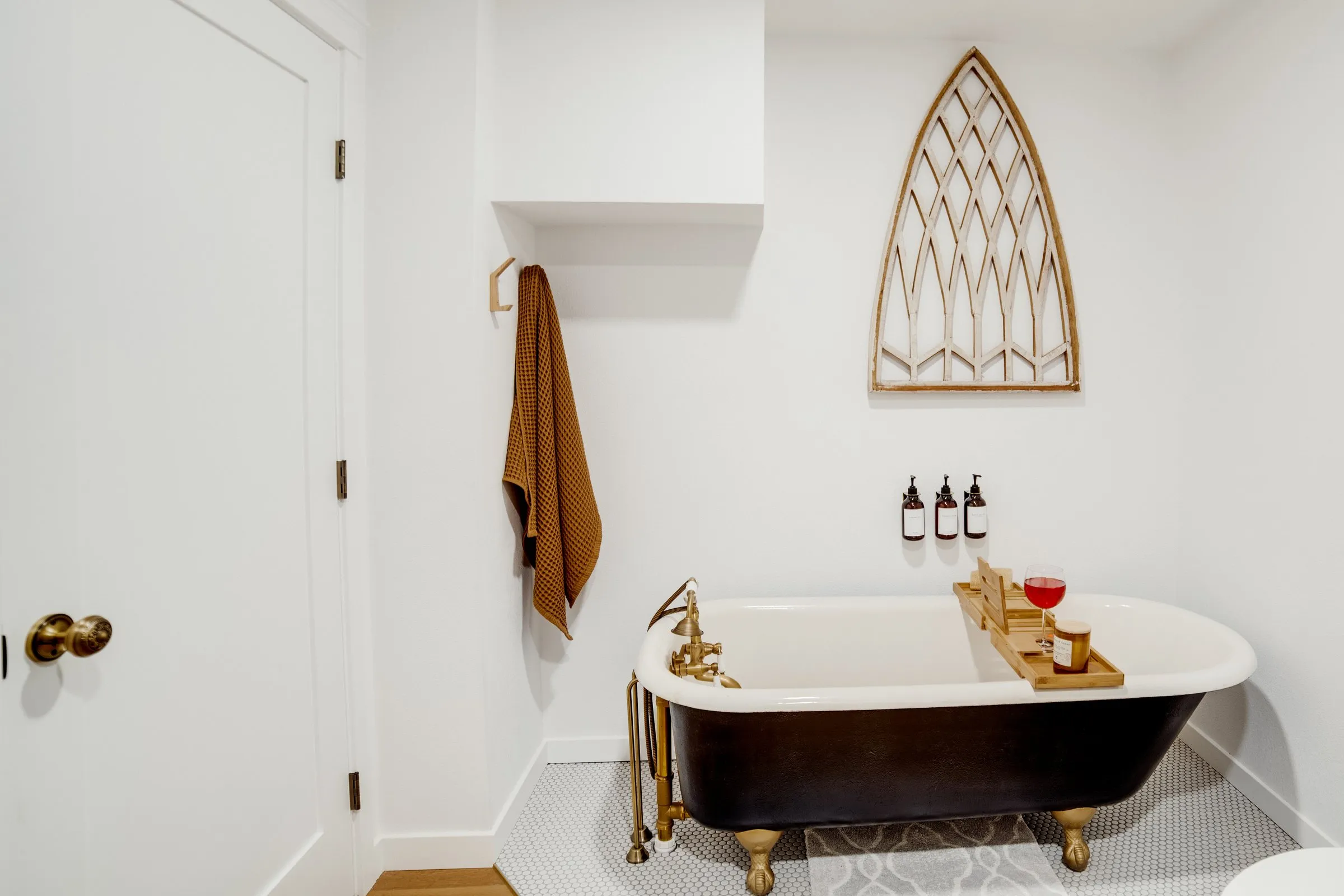 Black clawfoot soaking tub with brass fixtures and a bath caddy holding a glass of wine
