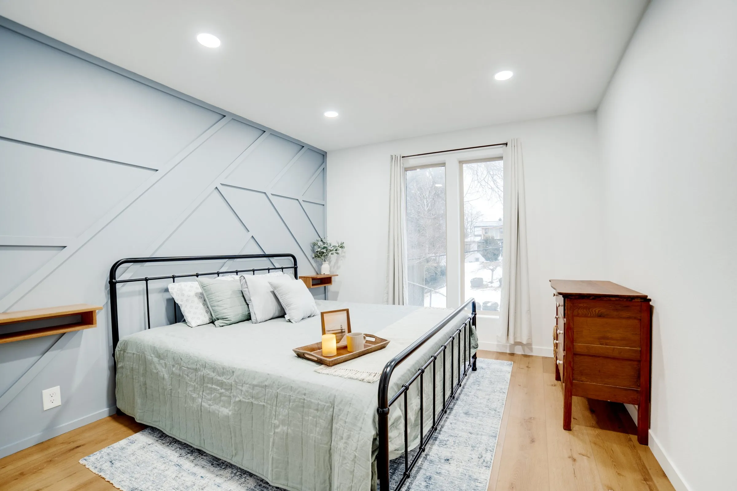 Main-floor bedroom with an iron bed, sage bedding and geometric accent wall